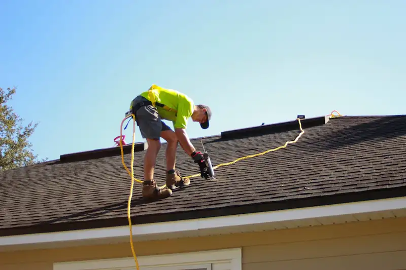 Roofer installing new shingles with a nail gun